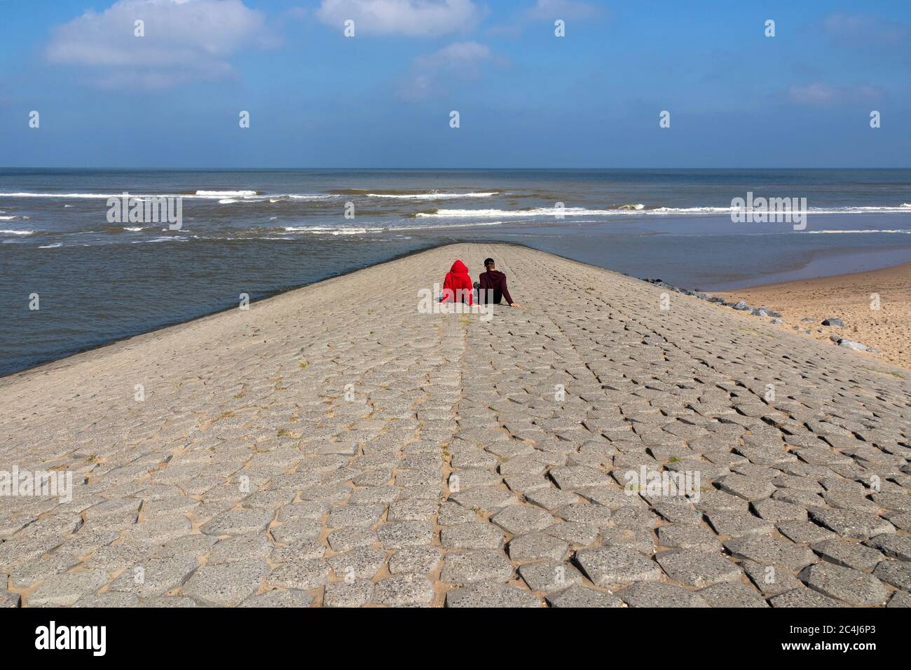 Coppia che guarda al Mare del Nord seduto sulle pietre di un molo in una bella giornata Foto Stock