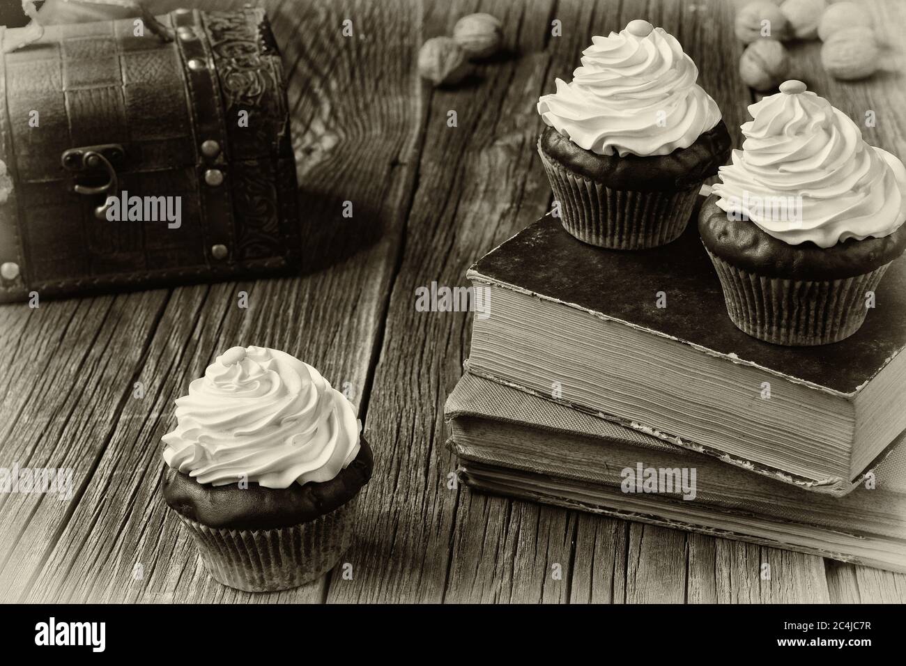 Cupcakes in cartoni patty sono giacenti su vecchi libri e tavole di legno stagionato. Un petto e qualche guscio di noce... un effetto foto bianco e nero. Foto Stock