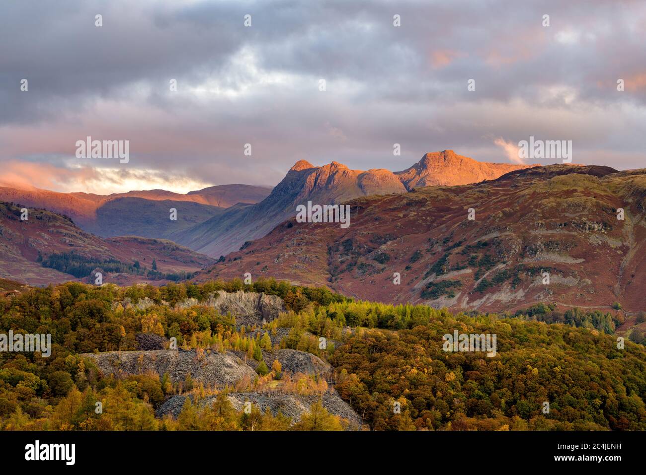 La catena montuosa Langdale Pikes all'alba, mentre la luce del mattino si illumina dalle nuvole scure Moody. Lake District, Regno Unito. Foto Stock