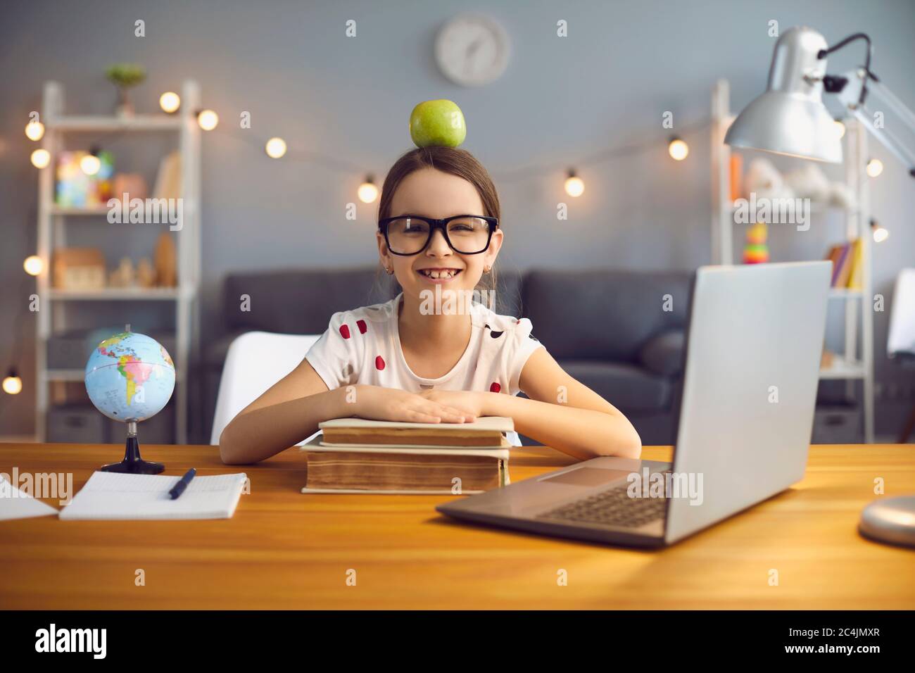 Divertente ritratto di sorridente scuola ragazza che studia online in salotto, homeschooling con computer portatile. Foto Stock