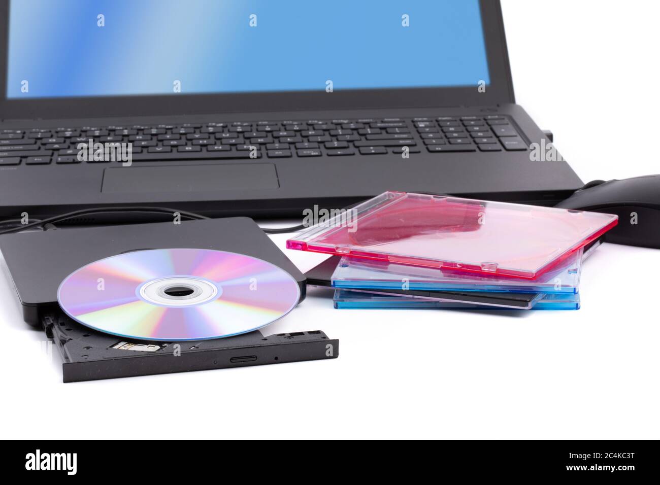 Un'unità CD DVD esterna per computer aperta con una pila di custodie per CD e un computer portatile in background Foto Stock