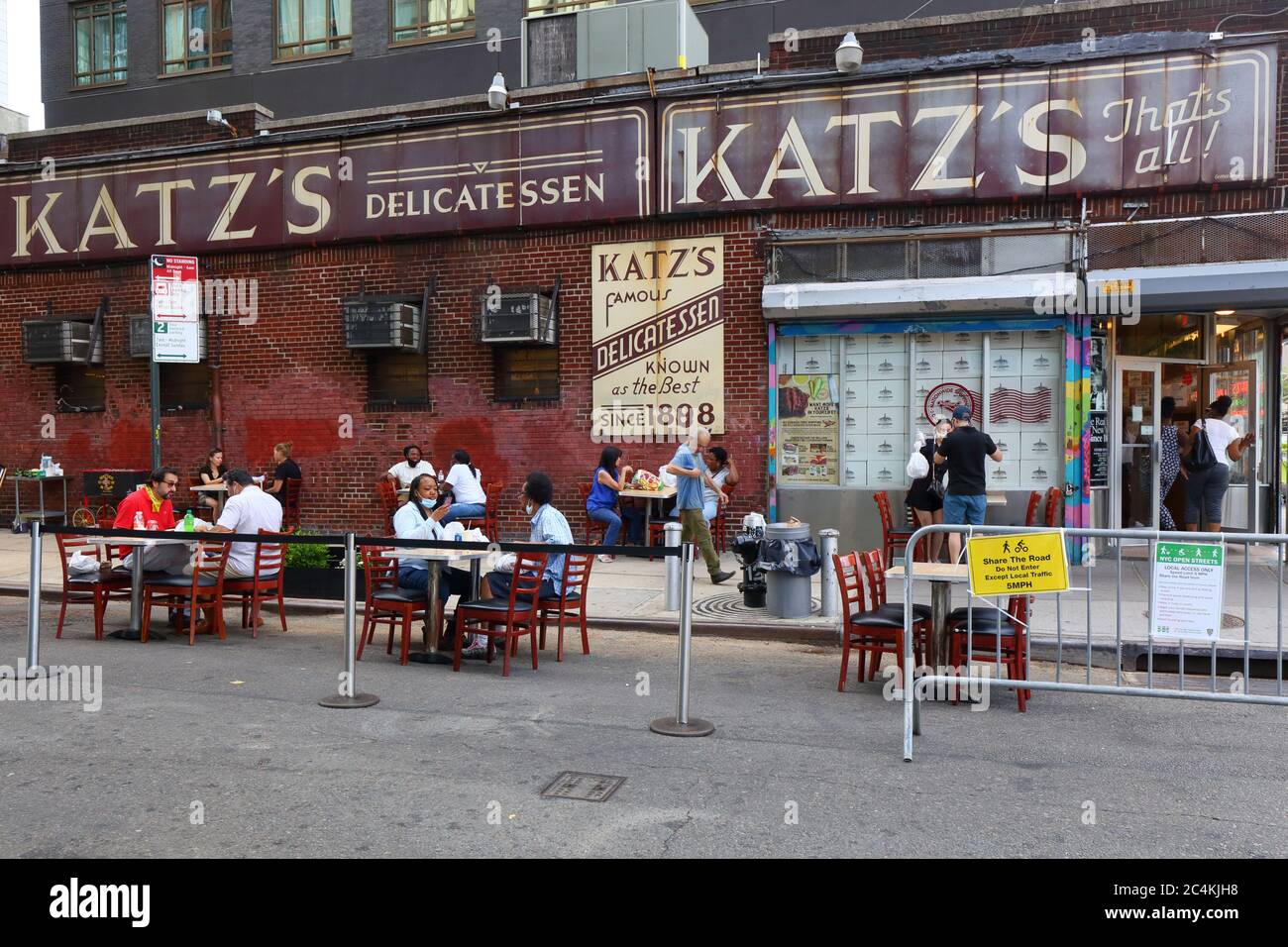 New York, New York. 25 giugno 2020. Cena all'aperto socialmente distanziata al Katz's Delicatessen su Ludlow Street a Manhattan, sotto la seconda fase di riapertura di New York City. Alcuni ristoranti e bar hanno una capacità maggiore convertendo i corridoi di parcheggio in parchi, marciapiedi estensioni sulla strada per ristoranti e per il tempo libero, e non per il deposito auto. Alcune strade del Lower East Side sono state chiuse al traffico sotto la seconda incarnazione di New York Open Streets, consentendo una cena più rilassante. Il traffico in strade aperte 2.0 non è imposto dalla polizia e si basa sulle imprese, le persone e la messa in atto Foto Stock