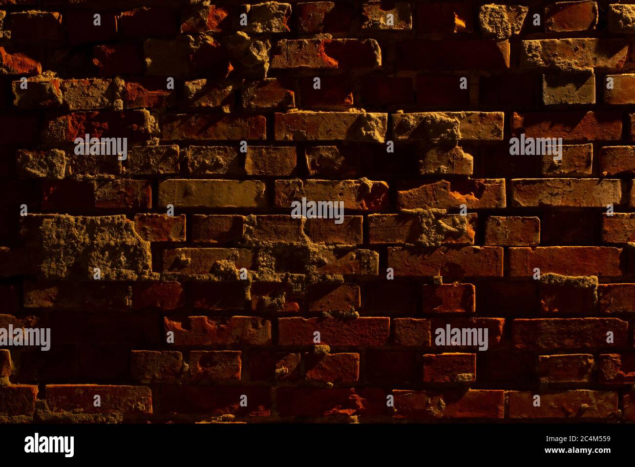 Vecchia grugia e muro di mattoni rossi danneggiato di notte con luce di una lanterna che splende su di essa Foto Stock