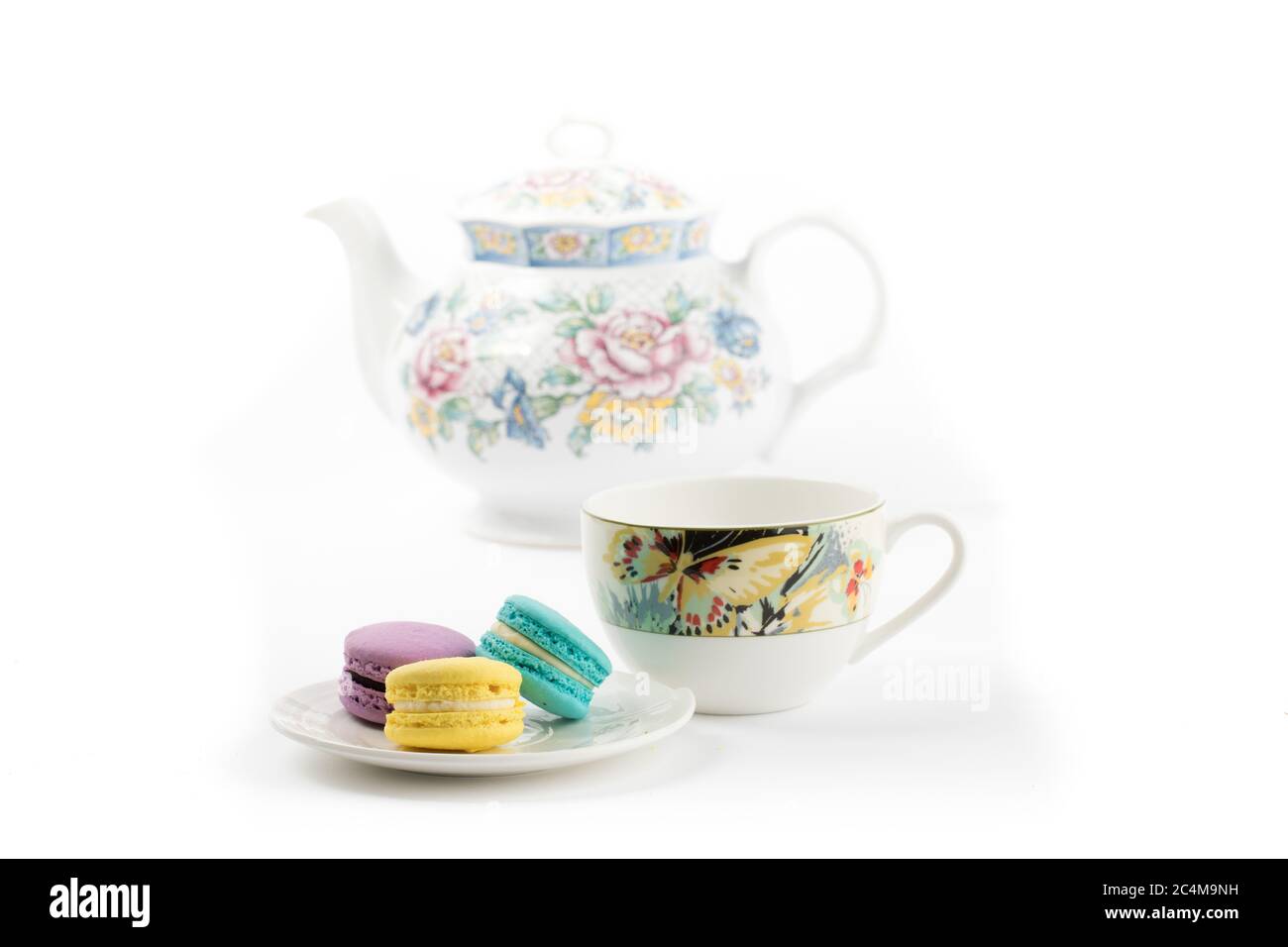 un piatto di biscotti colorati con un teacup e una teiera su sfondo bianco Foto Stock