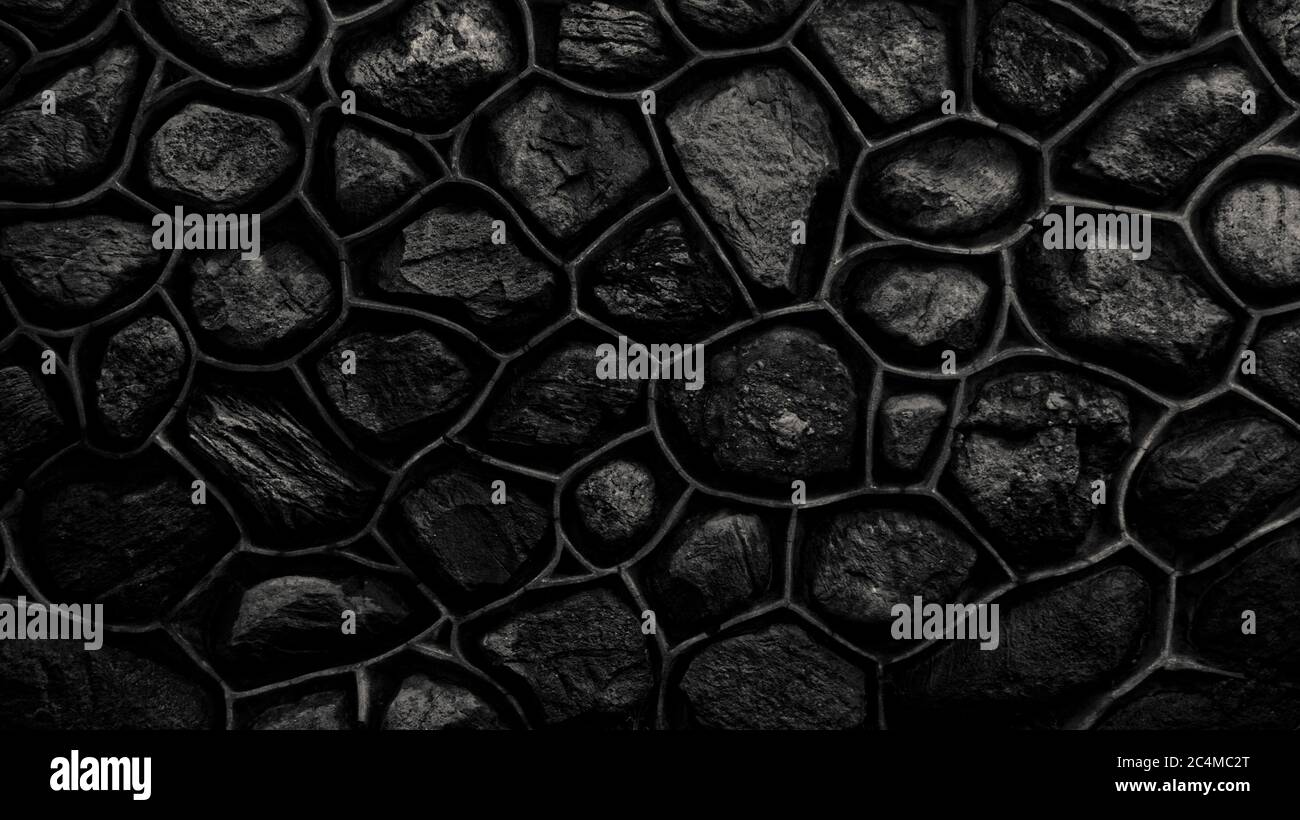 Parete monocromatica scura in pietra e cemento. Mosaico di rocce usate come tessere. Recinzione di pietra nera. Struttura decorativa in materiale naturale. Sfondo Foto Stock