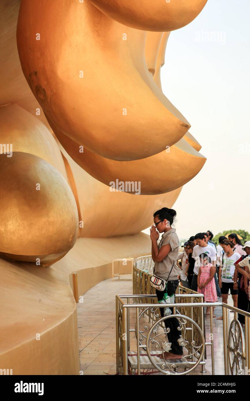 I fedeli pregano alla base della statua del Buddha presso il tempio Wat Muang, il luogo sacro di culto buddista nella provincia di Ang Thong, a 120 km da Bangkok. E' la statua del Buddha più alta del regno, alta 92 metri e larga 63 metri. Foto Stock