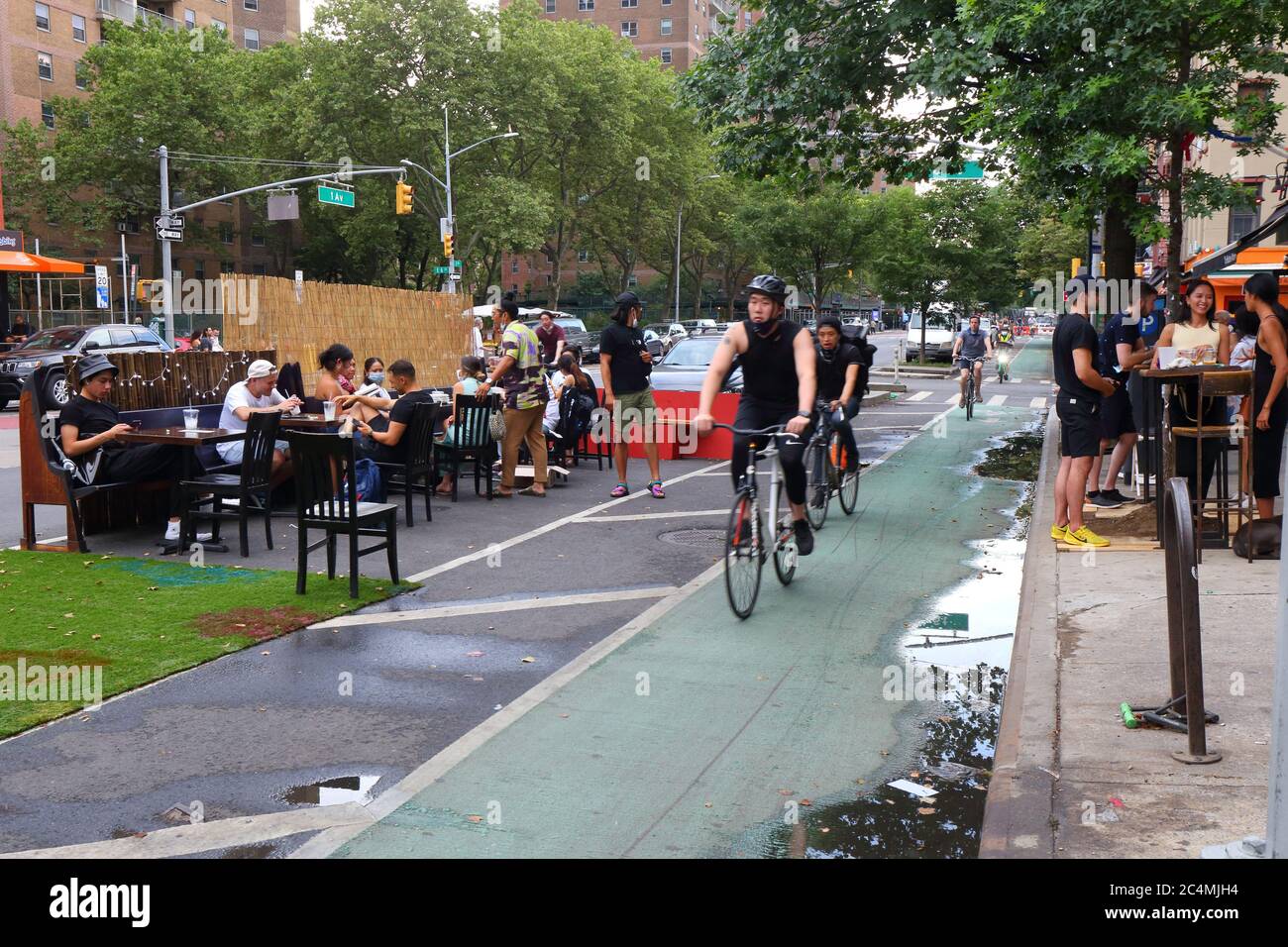 New York, New York. 27 giugno 2020. Persone in un locale da pranzo indipendente tra la pista ciclabile e il traffico in auto sulla First Avenue nel quartiere di East Village di Manhattan. I parcheggi sono estensioni laterali su una corsia di parcheggio di una strada o di una strada per aumentare lo spazio pubblico. Con la riapertura della fase 2 di New York City che consente ai ristoranti di servire i clienti, i parchi vengono utilizzati per cene all'aperto socialmente distanziate. Questo particolare parco è situato in una corsia di parcheggio galleggiante. Foto Stock