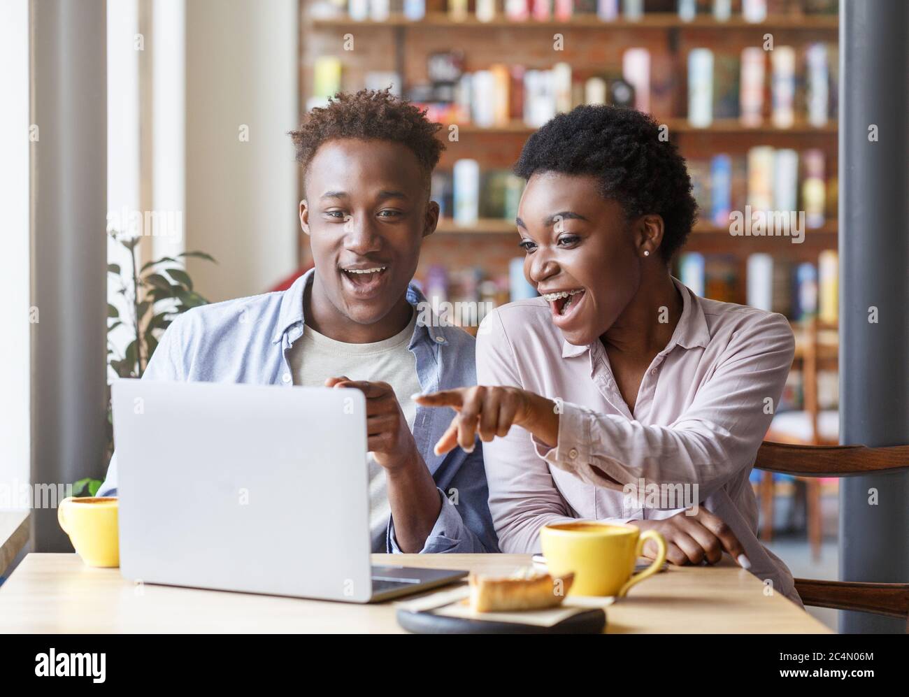 Una coppia nera gioiosa che guarda insieme film divertenti su un computer portatile presso la caffetteria Foto Stock