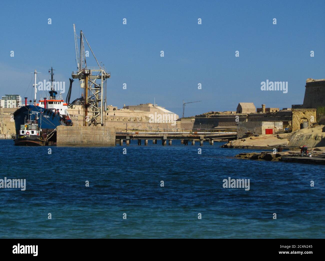 KALKARA, MALTA - 19 aprile 2014: L'industria di impianti di pulizia delle navi cisterna a Rinella Bay, Kalkara, parte di Fort Ricasoli, Malta, in funzione con il mare blu Foto Stock