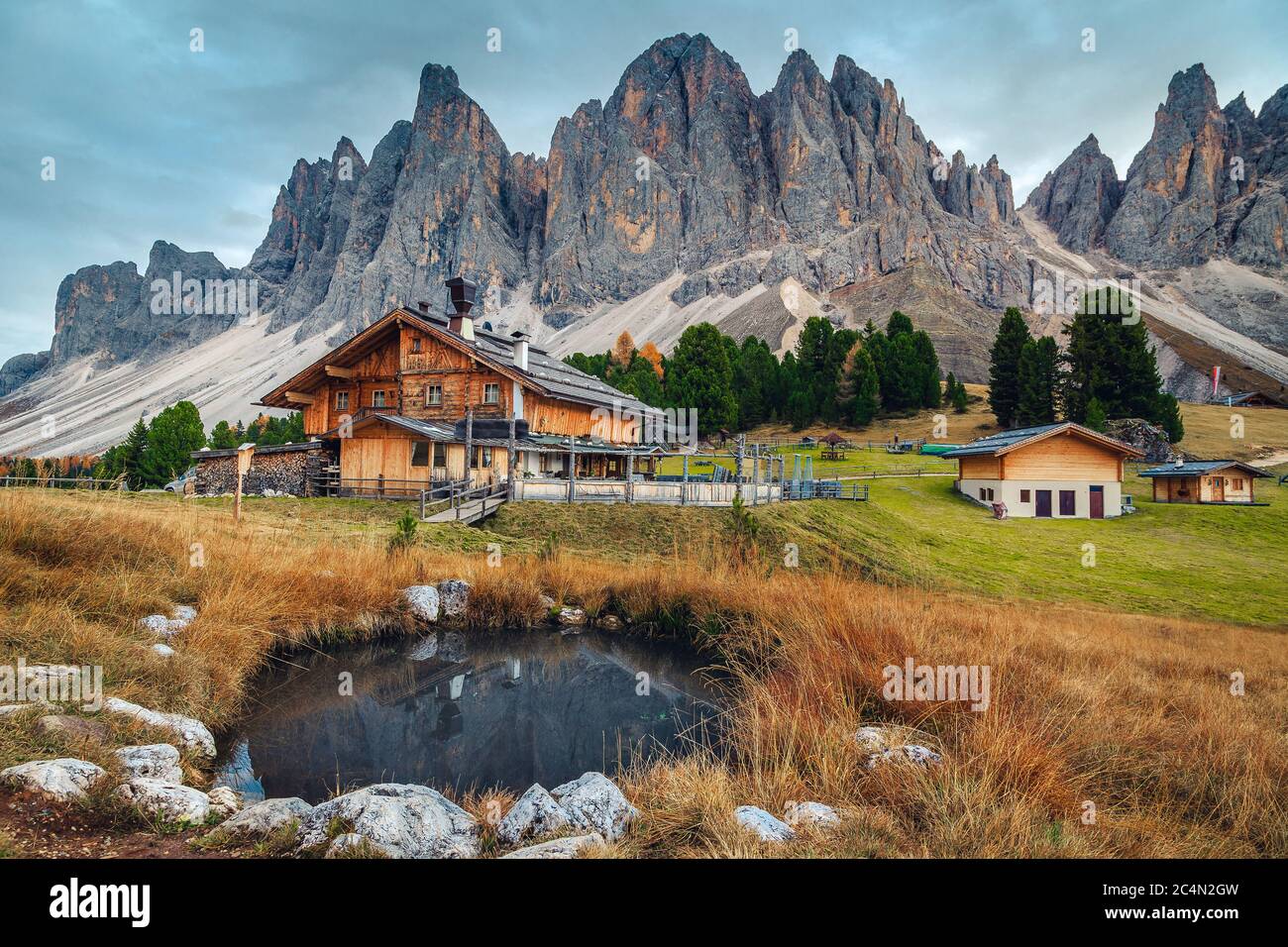 Pittoresco paesaggio alpino autunnale, graziosi chalet in legno e piccolo lago con alte montagne sullo sfondo, gruppo di Geisler - Odle, Alto Adige, Foto Stock