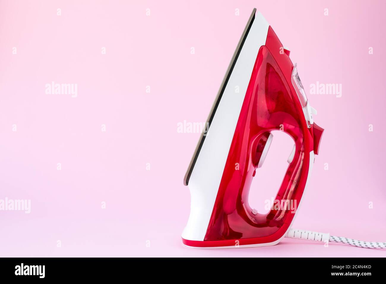 Ferro rosso di plastica su sfondo rosa. Apparecchi per stirare, concetto domestico. Modello con spazio di copia, posto vuoto per il testo Foto Stock