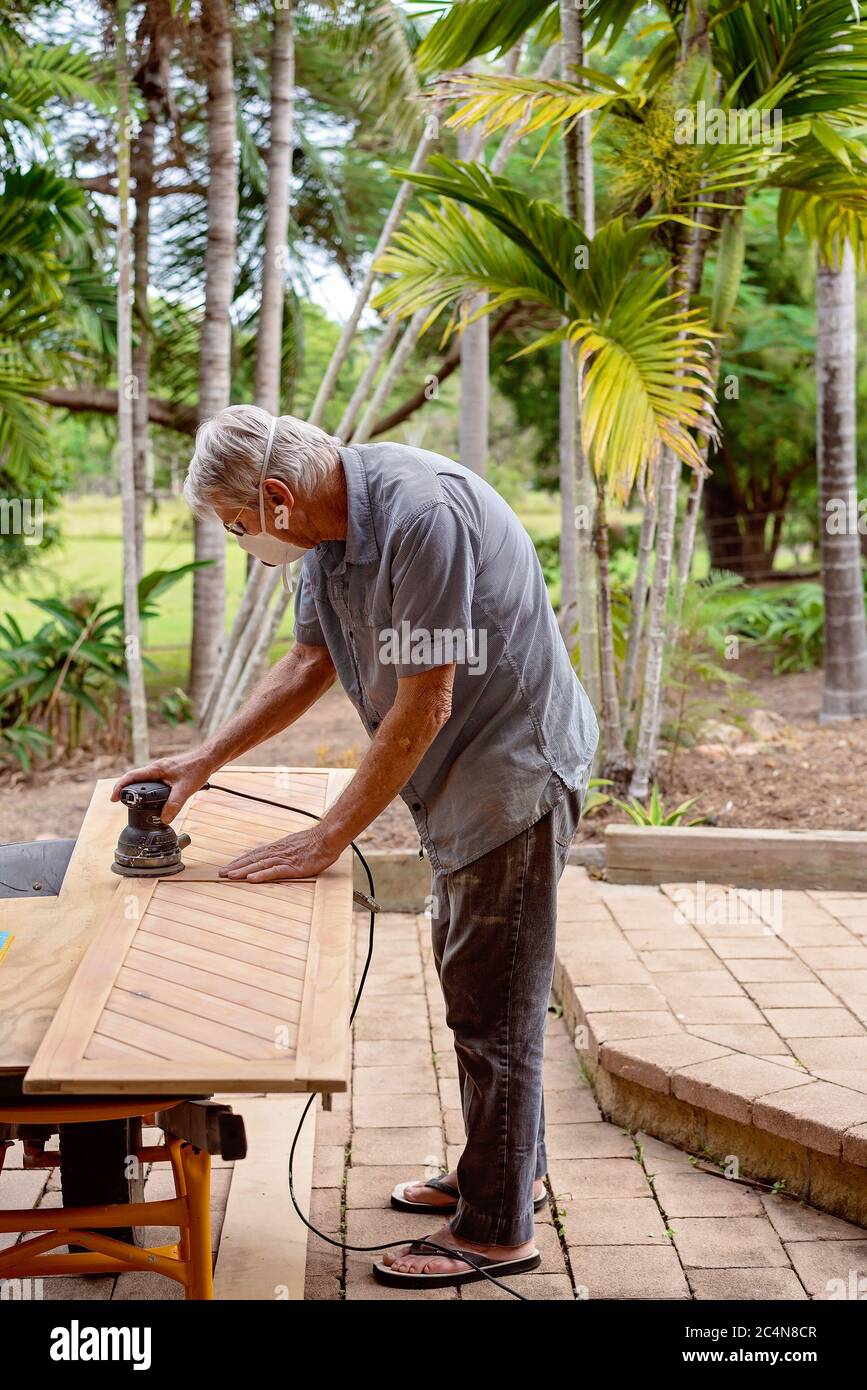 Townsville, Queensland, Australia - Giugno 2020: Sabbie senior dai capelli grigi giù porta armadio in legno pronto per la pittura come un progetto di handyman domestico Foto Stock