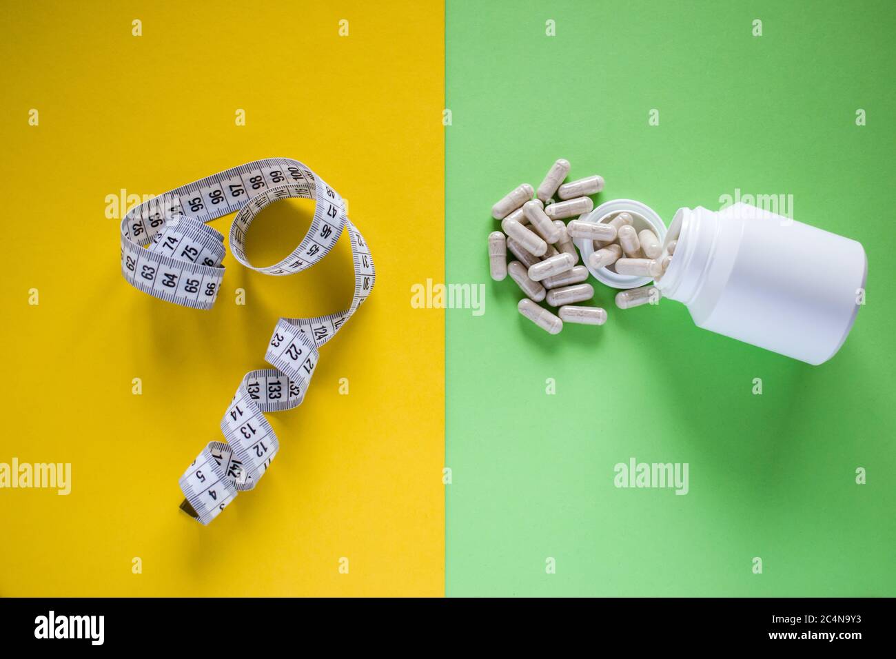Metro a nastro e pillole mediche su sfondo giallo e verde diviso Foto Stock