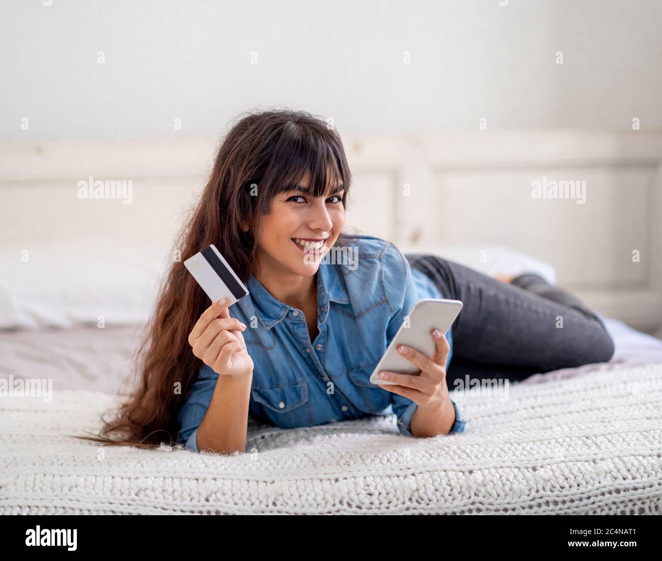 Focolaio COVID-19. Spegnimento e shopping online. Giovane donna attraente con carta di credito utilizzando smartphone mobile acquistare cibo su Internet a casa d Foto Stock