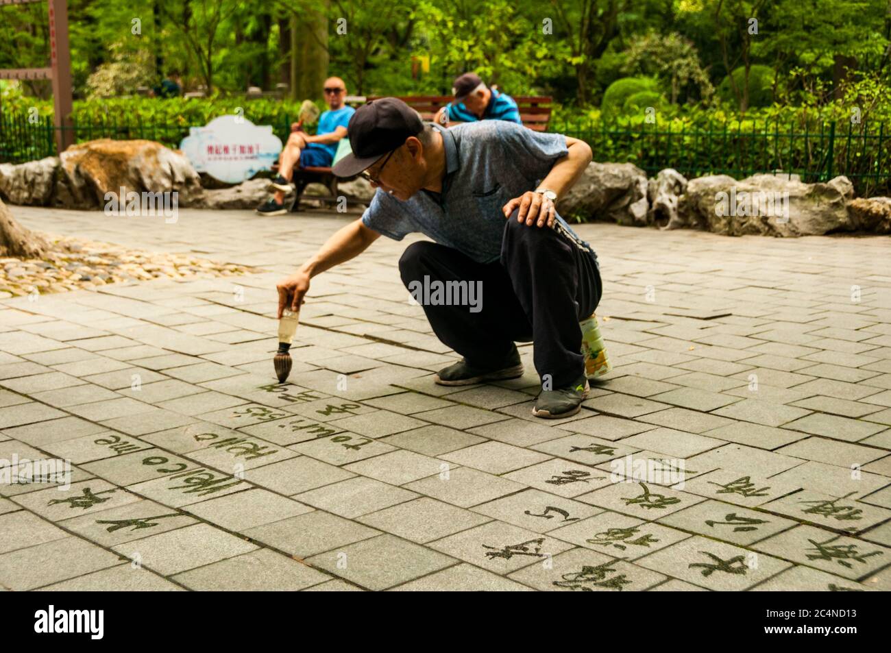 Un vecchio scrive la calligrafia usando un pennello ad acqua nel Parco Lu Xun di Shanghai. Foto Stock