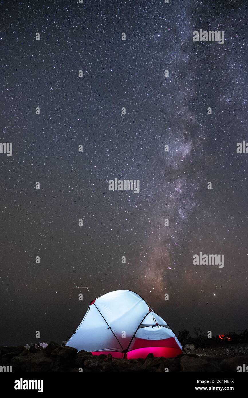 Una tenda si illumina sotto un cielo notturno pieno di stelle. Foto Stock