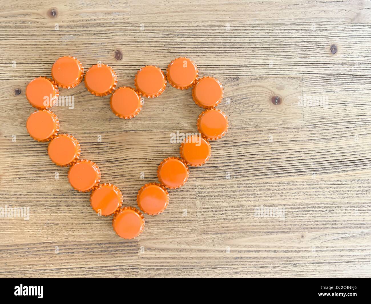 Un cuore d'amore arancione fatto di birra bottiglie di coperchi su un rustico tavolo di legno. Bevitori di birra concetto di San Valentino vista dall'alto immagine orizzontale con em Foto Stock