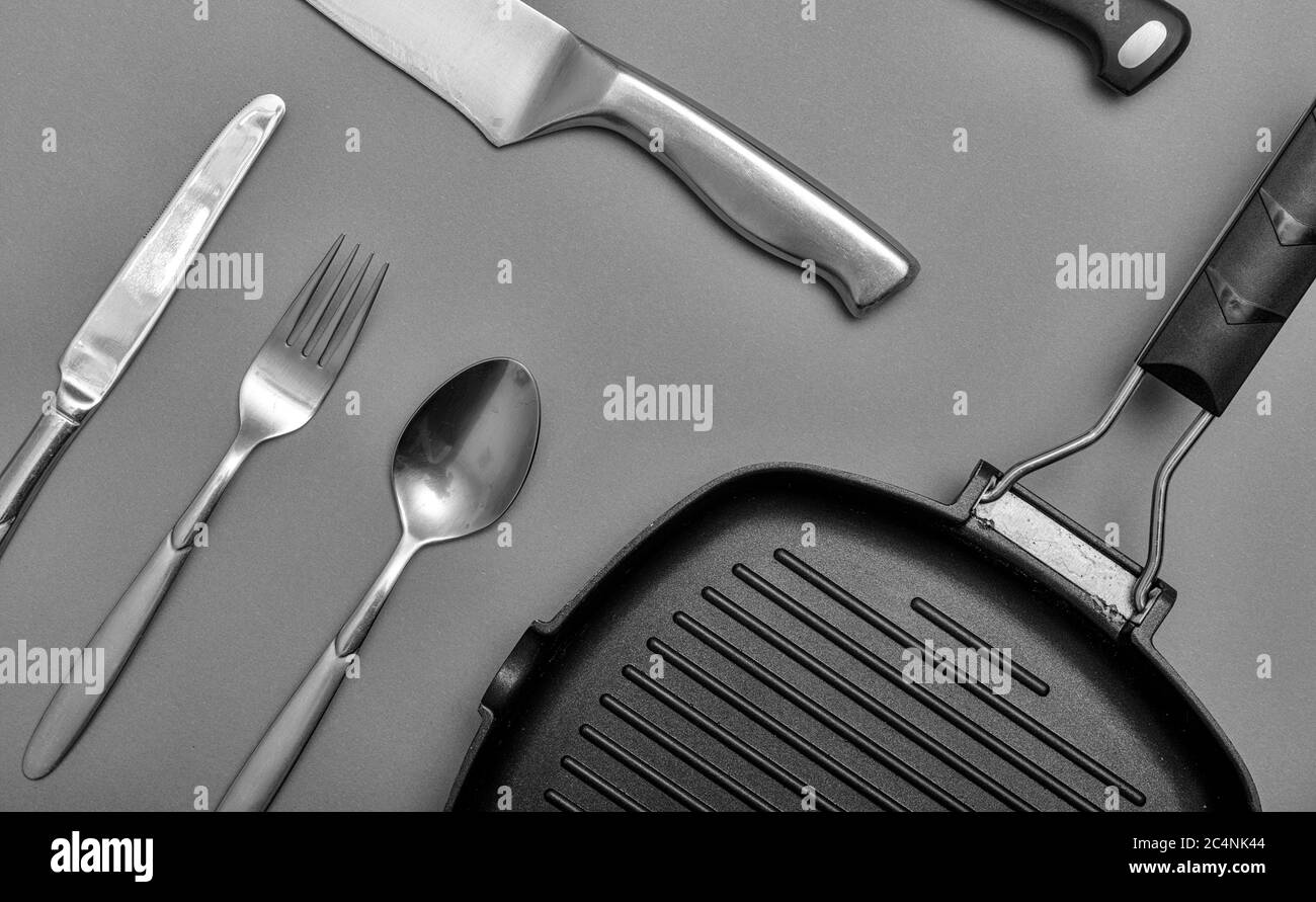 Coltelli in metallo con nero su un tavolo grigio, piatto grigliato, asciugamano. Disposizione piatta, layout con spazio di copia. Foto Stock