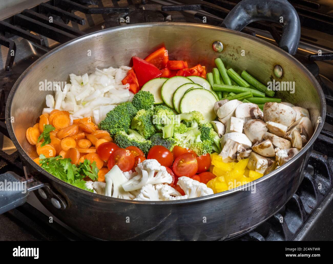 Una teglia rotonda in acciaio su un piano cottura, piena di verdure crude tagliate e tagliate a fette, pronta per essere cotte per la cena. Foto Stock