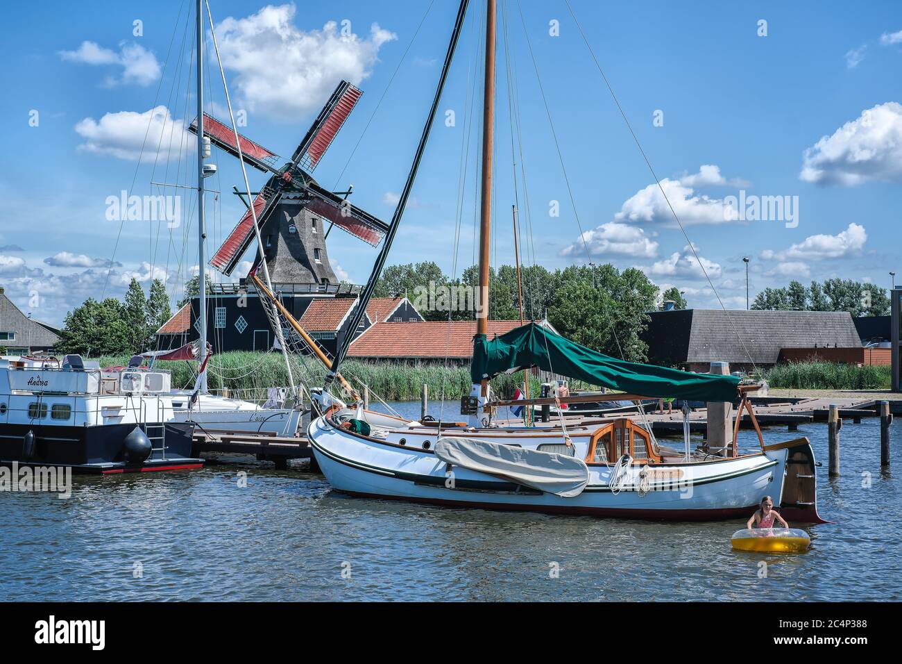 Europa, Paesi Bassi - Tour attraverso i canali di Friesland, un molo con una barca a vela, sullo sfondo un mulino a vento tradizionale Foto Stock