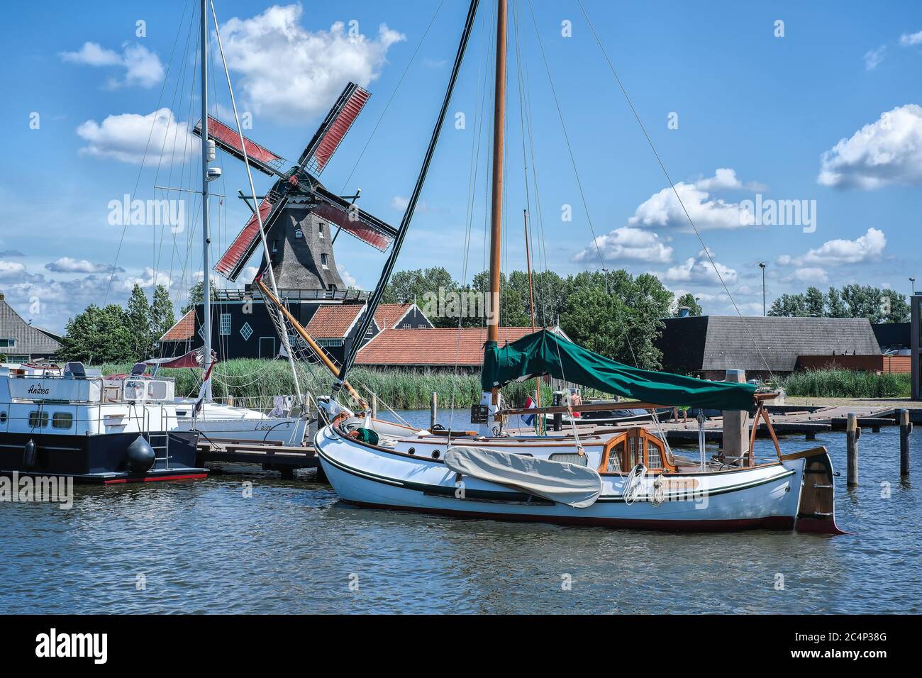 Europa, Paesi Bassi - Tour attraverso i canali di Friesland, un molo con una barca a vela, sullo sfondo un mulino a vento tradizionale Foto Stock