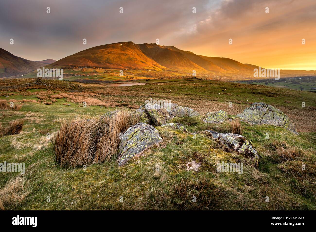 Bella luce dorata che si illumina sulle montagne all'alba con le rocce rugose in primo piano. Lake District National Park, Regno Unito. Foto Stock