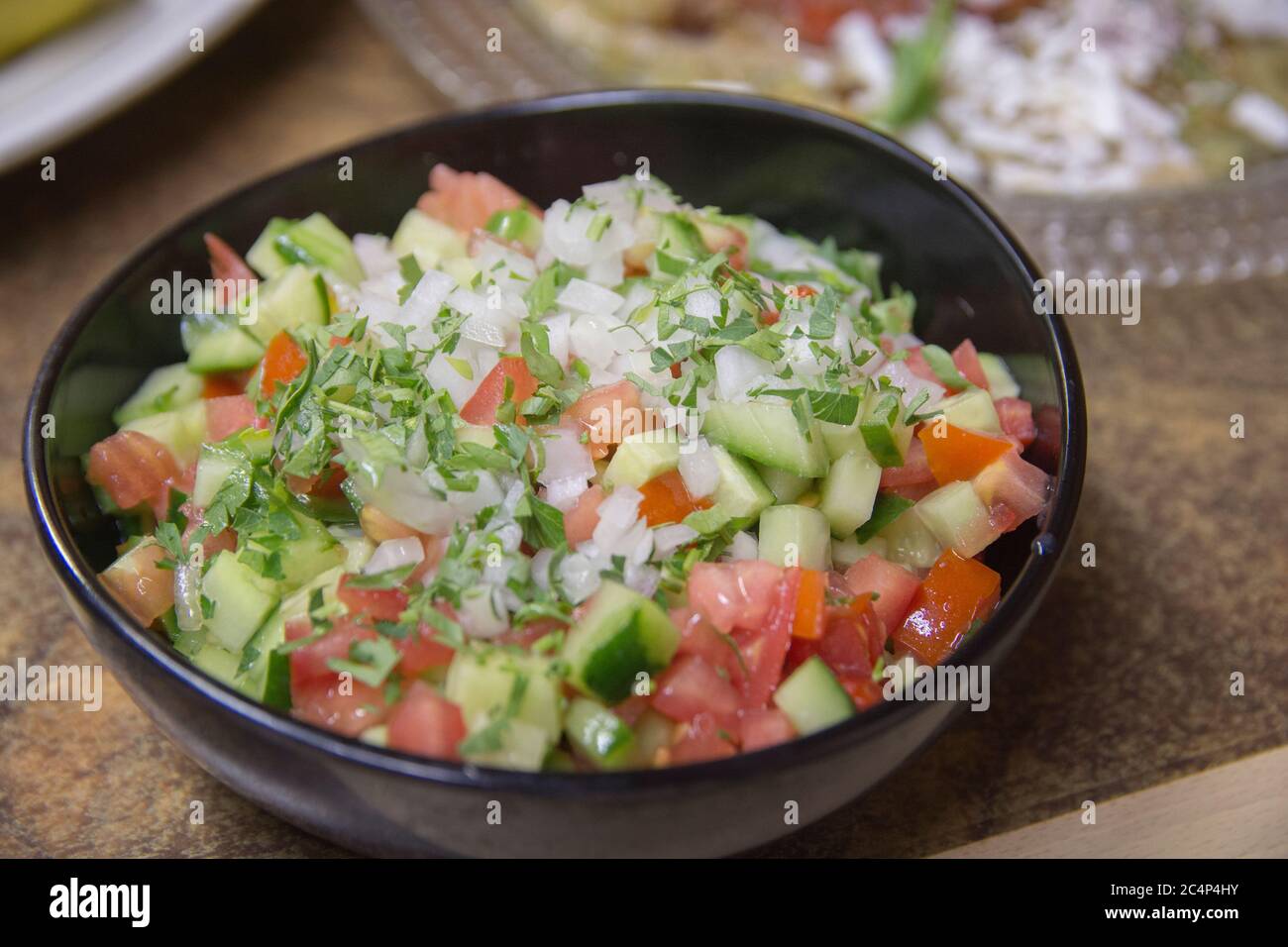 Insalata di verdure fresche israeliane, contenente cetriolo, cipolla bianca di pomodoro e prezzemolo, servita in un recipiente scuro Foto Stock