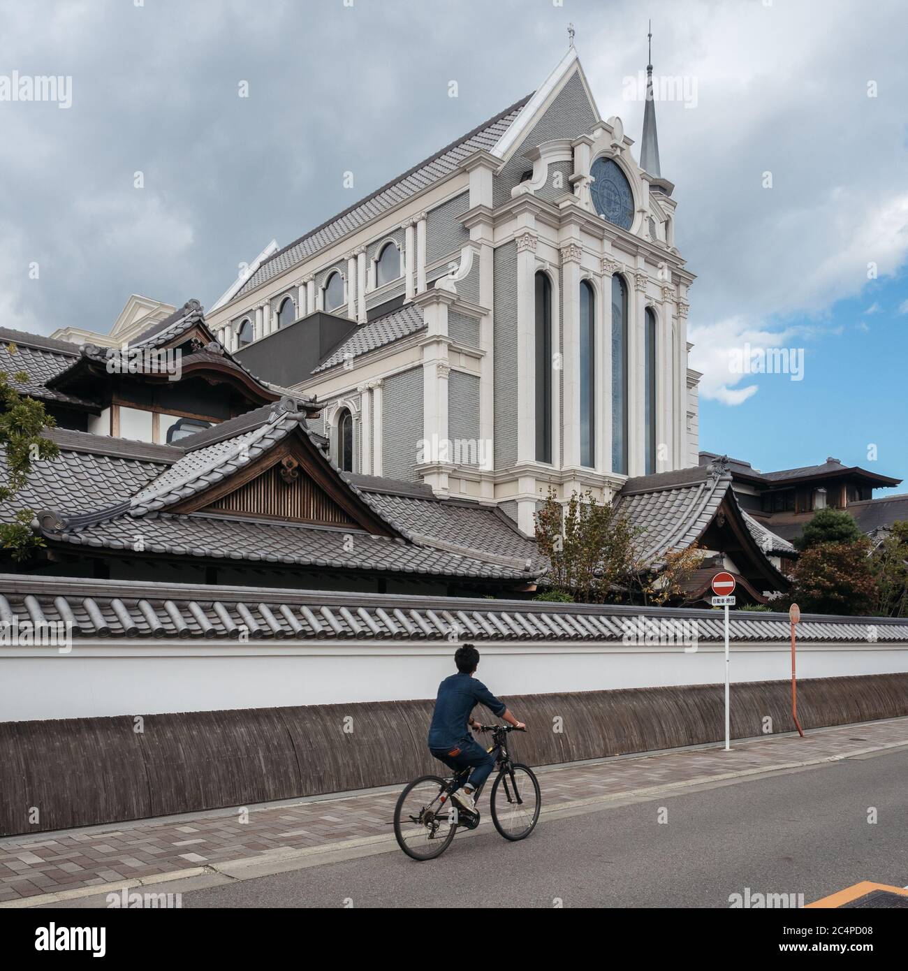 Nagoya, Aichi, Giappone - un uomo che cavalcano in bicicletta sullo sfondo del santuario giapponese e della chiesa cattolica. Fusione di stile architettonico orientale e occidentale. Foto Stock