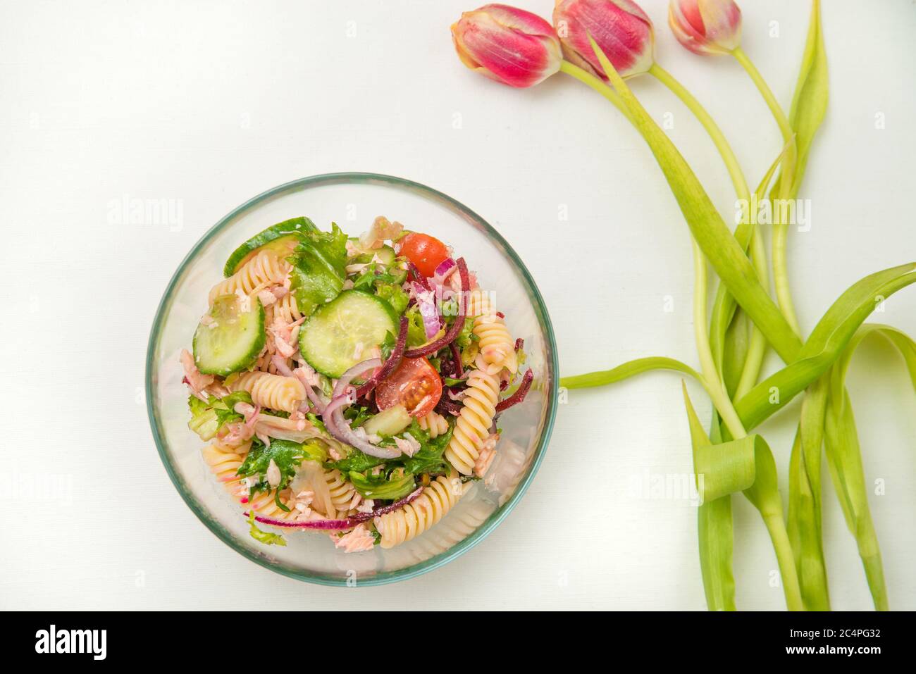 Una ciotola di insalata di pasta di salmone e alcuni fiori rossi di tulipani sullo sfondo. Foto Stock