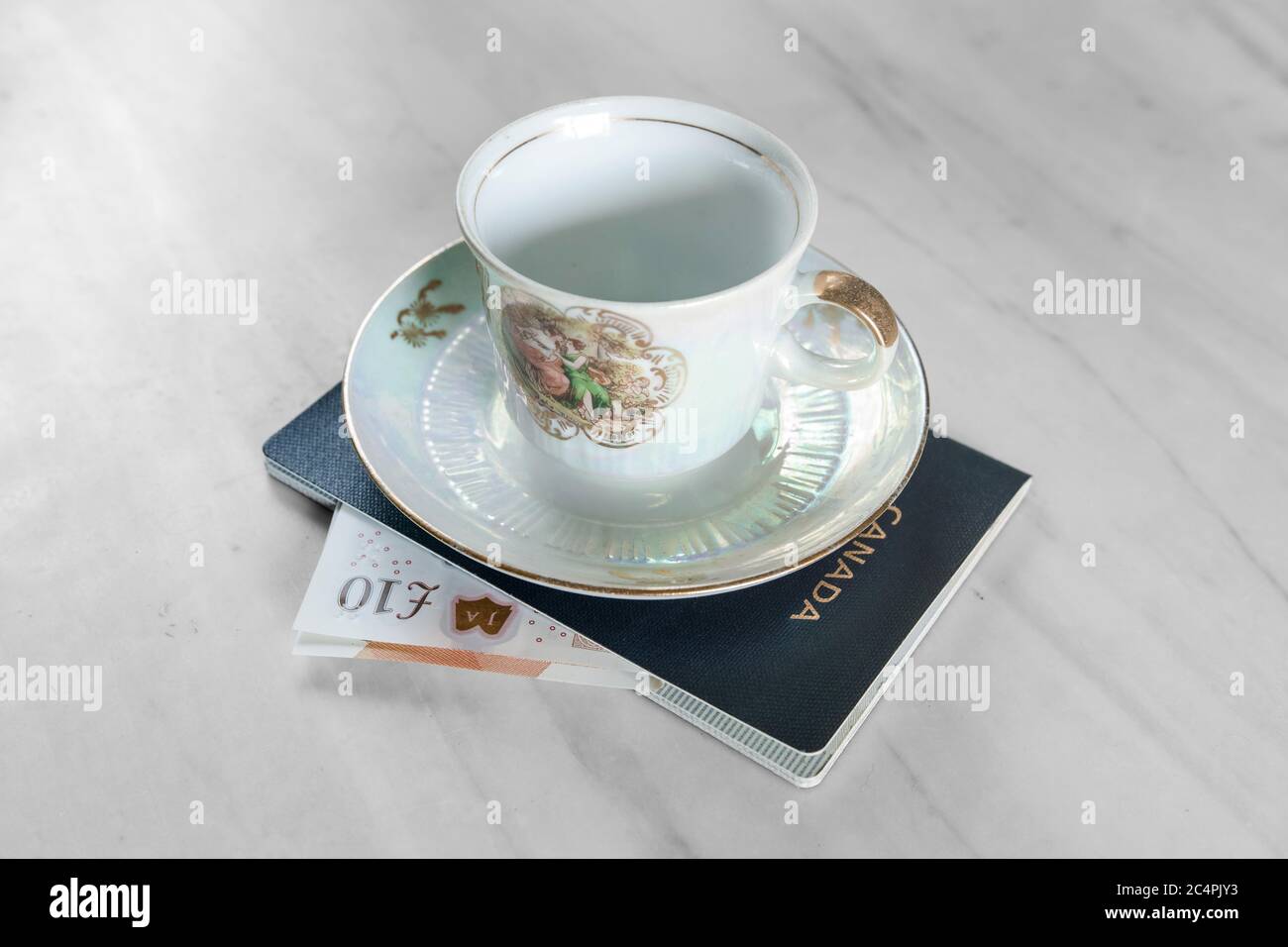 Sotto una tazza da tè decorata graziosamente, vediamo il passaporto canadese in cui è scivolato una banconota di 10 libbre del Regno Unito. Foto Stock