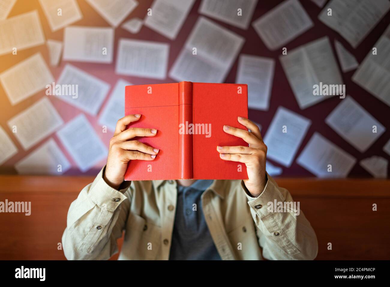 Lettore maschile che legge un libro rosso nella libreria. Lettura del concetto nella biblioteca. Foto Stock