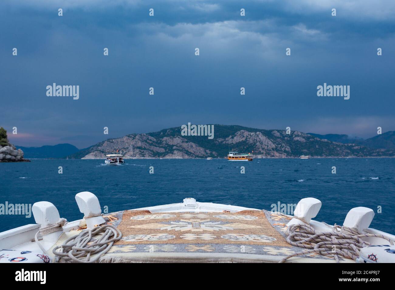 Vista dal prua di una barca a mare su barche, montagne e cielo tempestoso Foto Stock