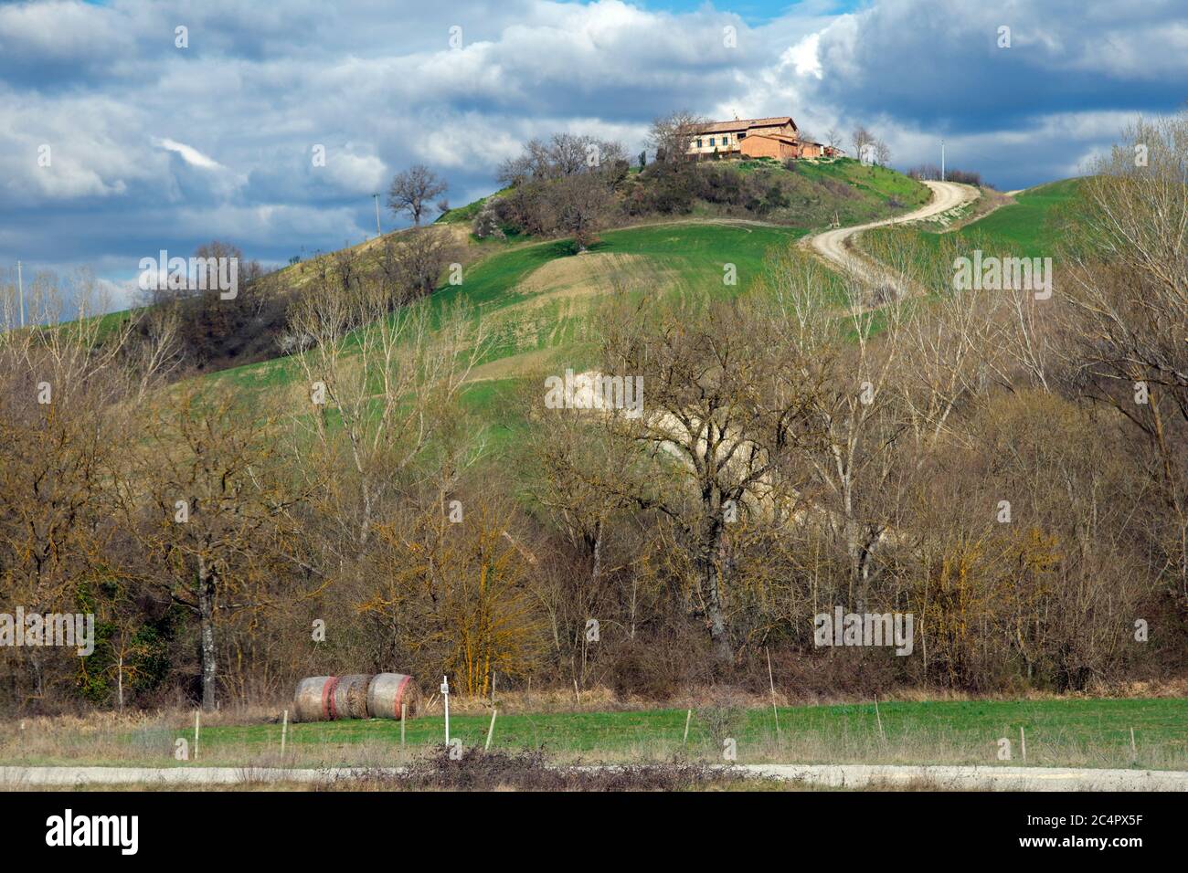 Piccole strade con cipressi mediterranei, casali e verdi colline, un paesaggio tipico della Toscana, Italia Foto Stock