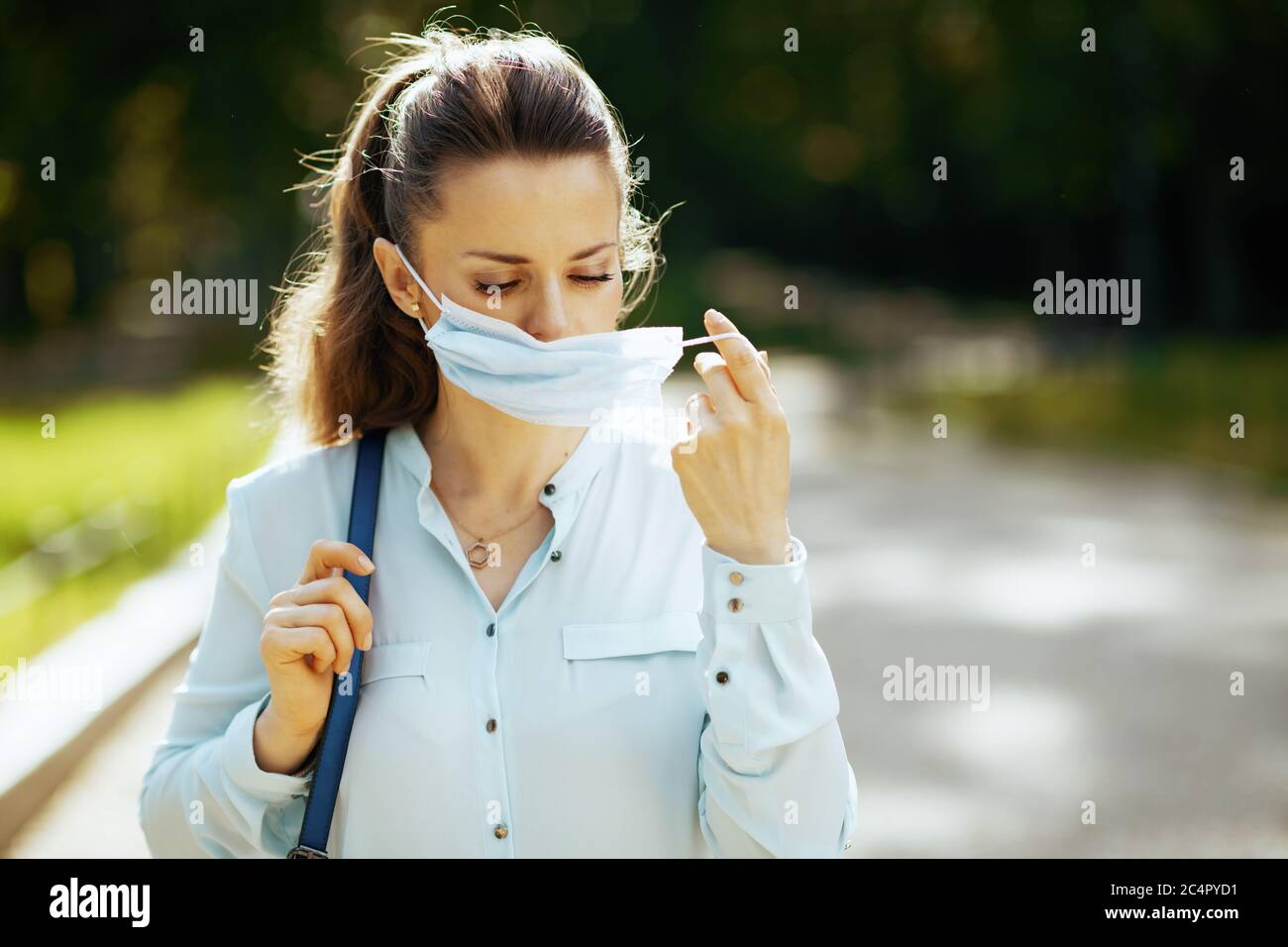 Vita durante la pandemia di covid-19. Donna moderna in blusa blu all'aperto nel parco della città con maschera medica. Foto Stock