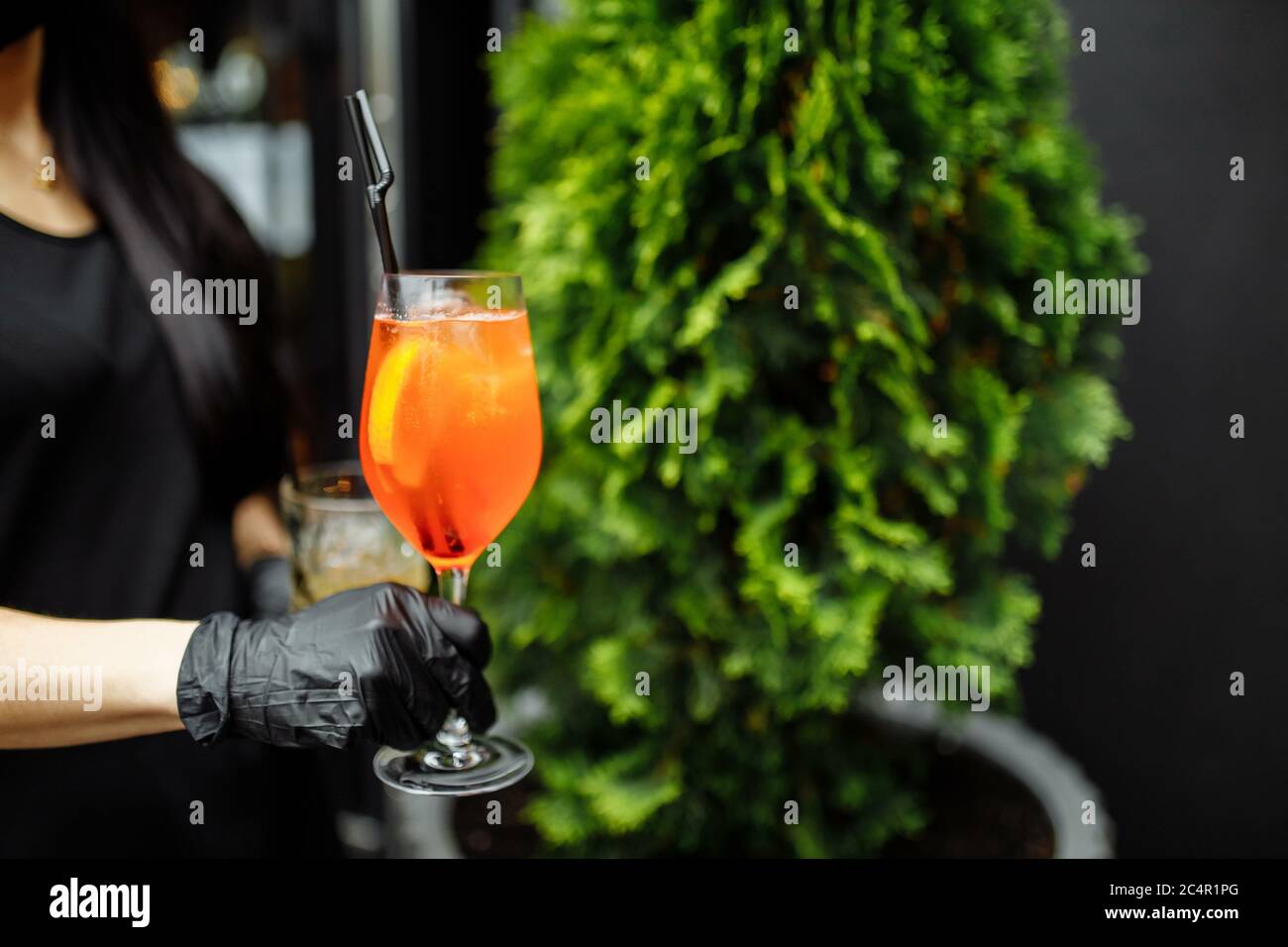 Cocktail aperol spritz luminoso e colorato in una mano cameriera in un guanto su uno sfondo di verde Foto Stock