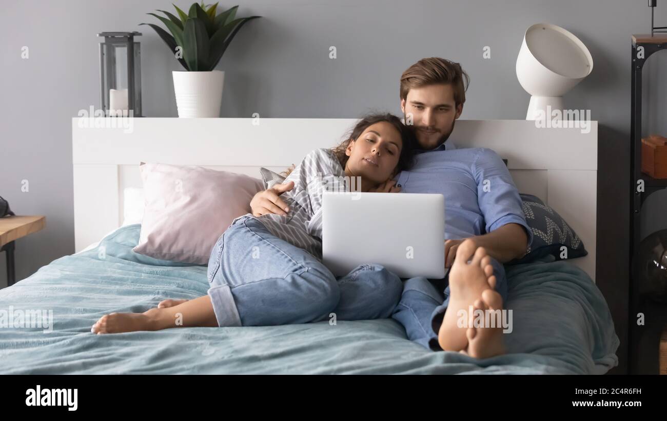 Giovane uomo e donna che si agguonano, rilassandosi a letto, usando il computer portatile Foto Stock