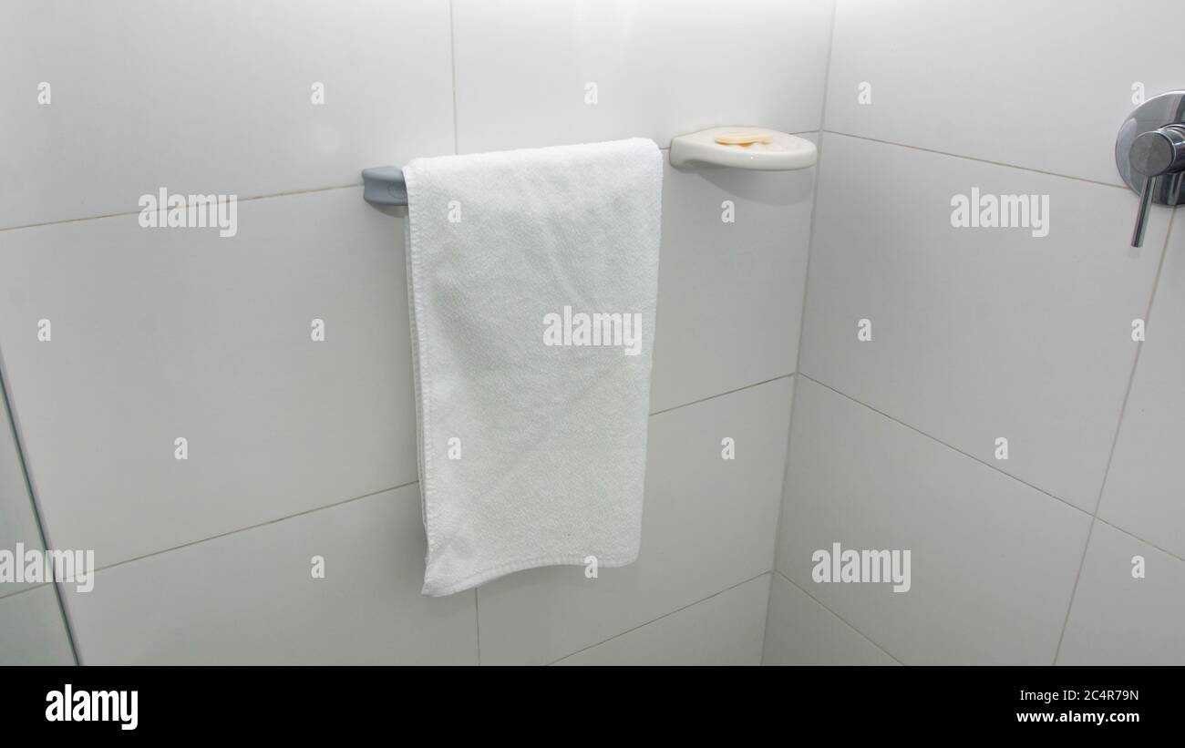 Un asciugamano bianco appeso su un porta-asciugamani in alluminio accanto a un sapone su un porta-sapone con una parete di fondo in ceramica bianca Foto Stock