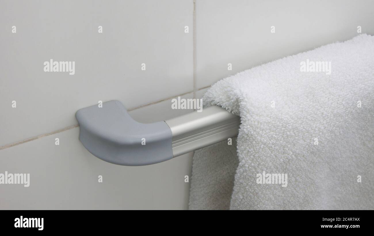 Asciugamano bianco appeso su un porta asciugamani in alluminio con una parete di fondo in ceramica bianca Foto Stock