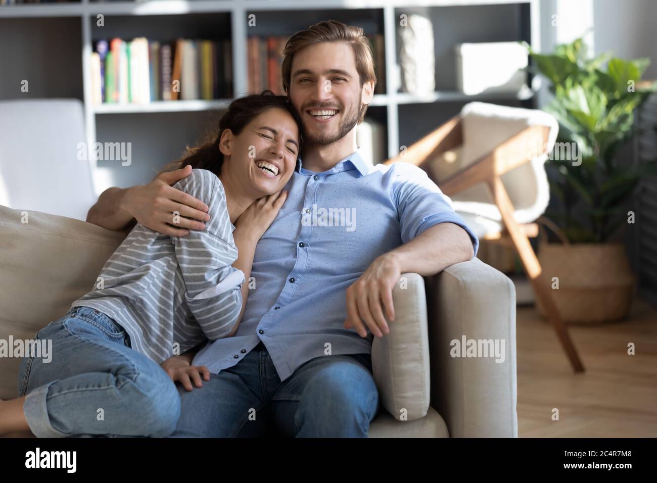 Felice giovane coppia abbracciando, ridendo di scherzo, seduto sul divano Foto Stock
