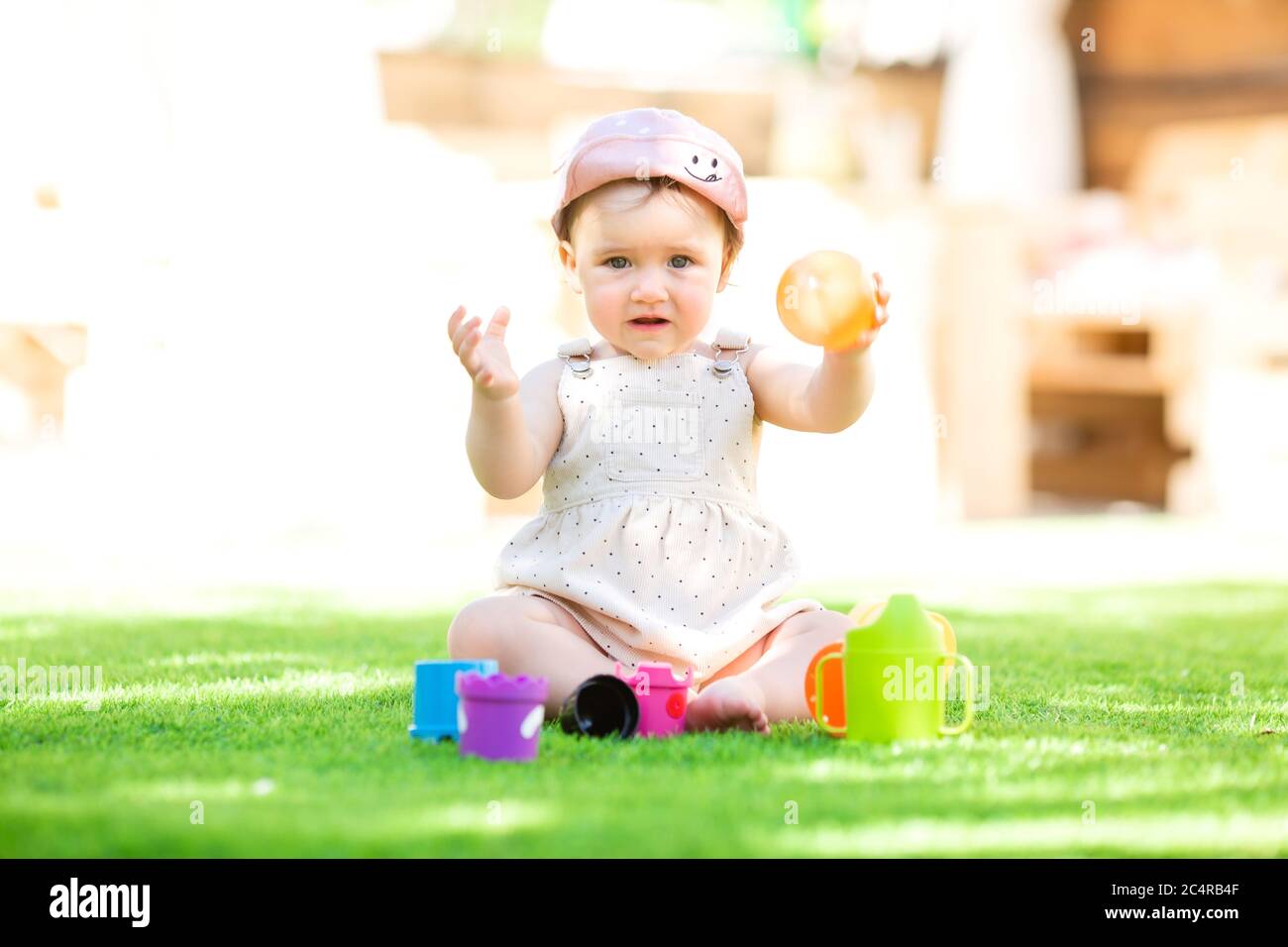 La bambina si siede in estate sul prato verde giocando in uno schema a piramide Foto Stock