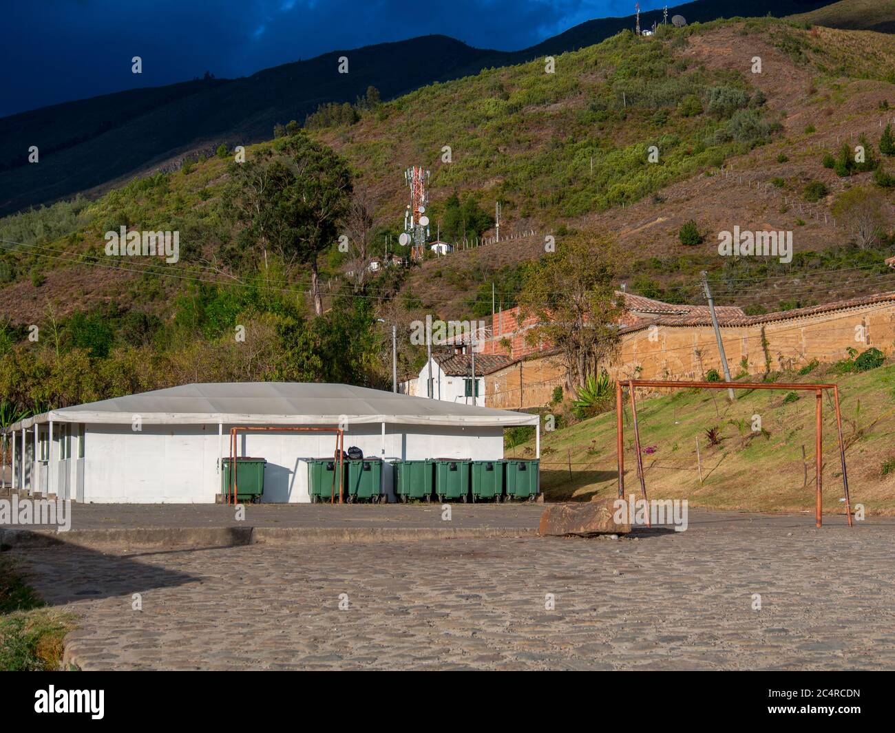 Vista panoramica di una linea di contenitori di rifiuti verdi contro un edificio bianco al mercato della città coloniale di Villa de Leyva, nella m andina Foto Stock