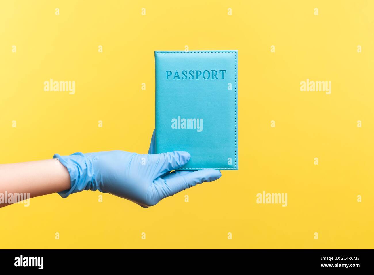 Profilo Vista laterale primo piano della mano umana in guanti chirurgici blu che tengono in mano il passaporto. Interno, studio shot, isolato su sfondo giallo. Foto Stock