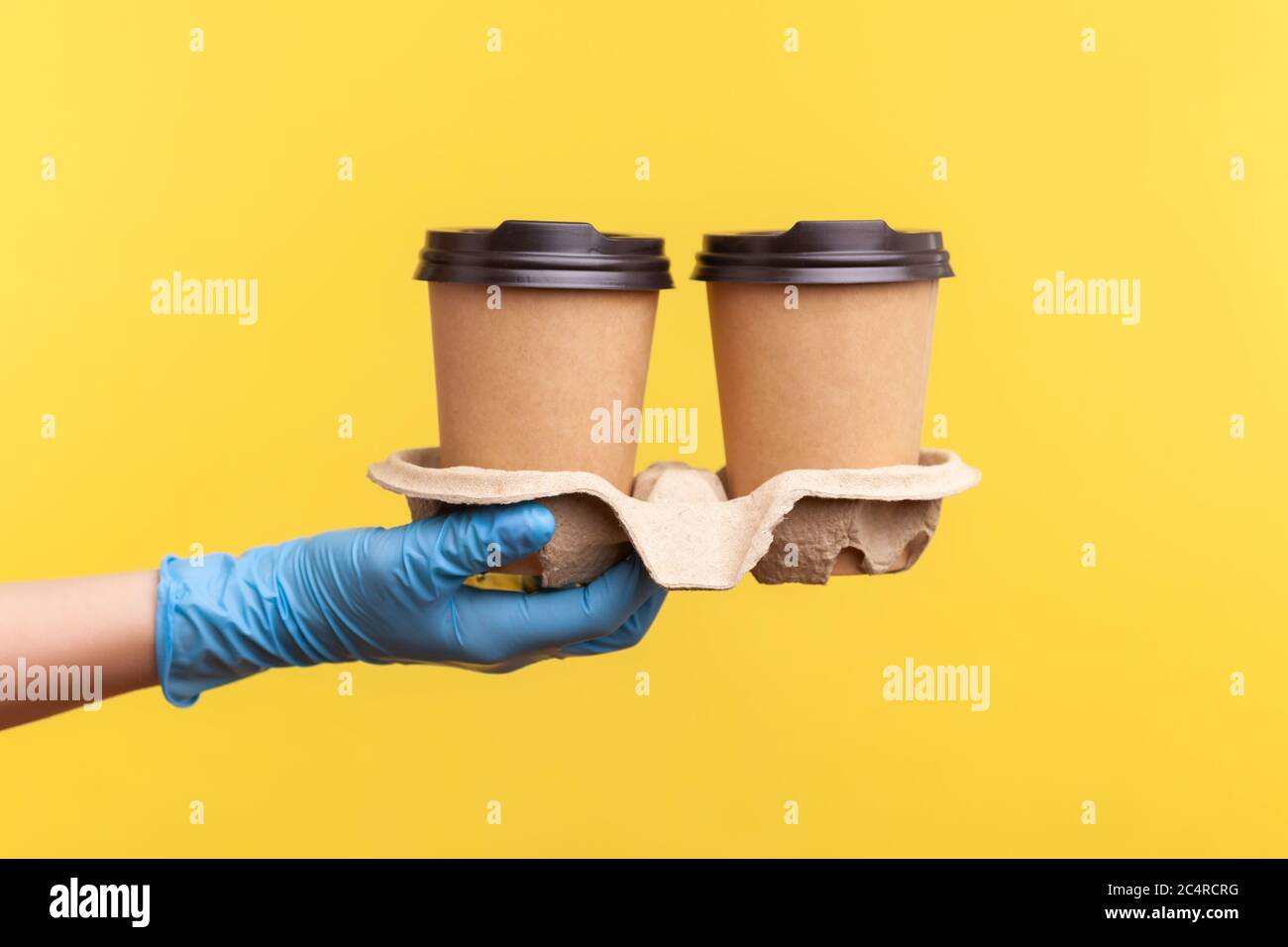 Profilo Vista laterale primo piano della mano umana in guanti chirurgici blu che tengono e mostrano tazze di tazza calda da asporto in mano. Interno, studio shot, isola Foto Stock