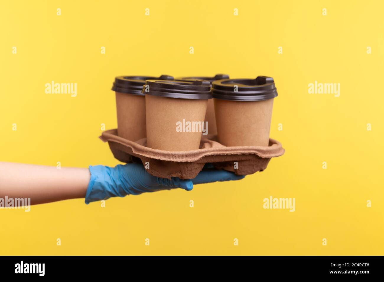 Profilo Vista laterale primo piano della mano umana in guanti chirurgici blu che tengono e mostrano tazze di tazza calda da asporto in mano. Interno, studio shot, isola Foto Stock