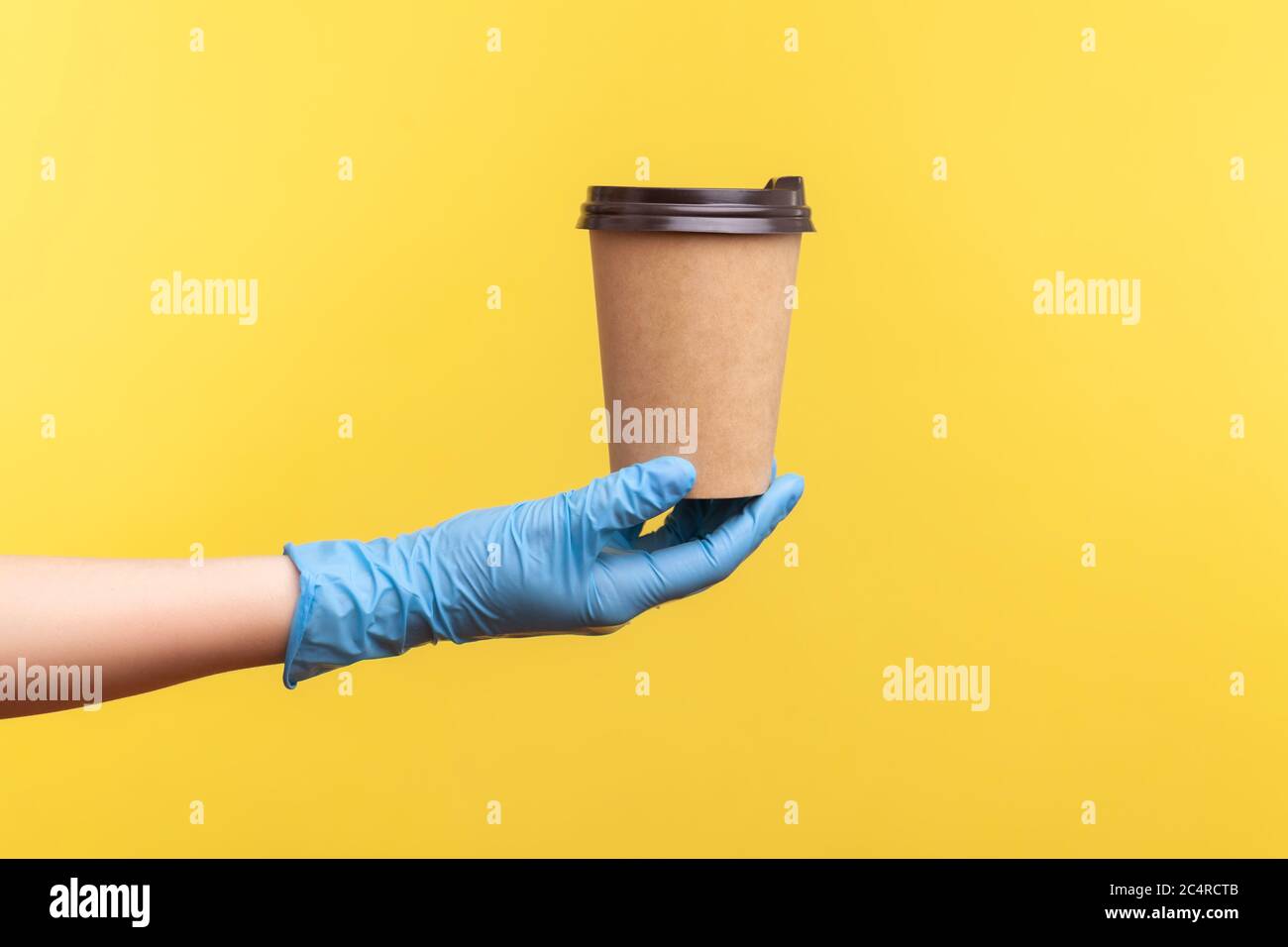 Profilo Vista laterale primo piano della mano umana in guanti chirurgici blu che tengono in mano e mostrano una tazza di tazza da takeaway calda. Interno, studio shot, isolat Foto Stock
