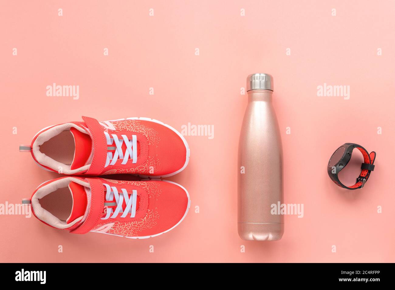 Sneakers rosse, orologio sportivo e bottiglia con acqua su sfondo rosa corallo. Concetto di vita sana, sport e formazione, vista dall'alto, spazio di copia. Foto Stock