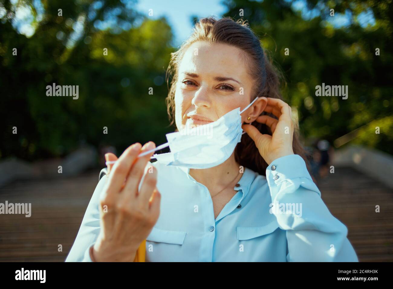 Vita durante la pandemia del coronavirus. Donna trendy di 40 anni in blusa blu all'aperto sulla strada della città che indossa la maschera medica. Foto Stock