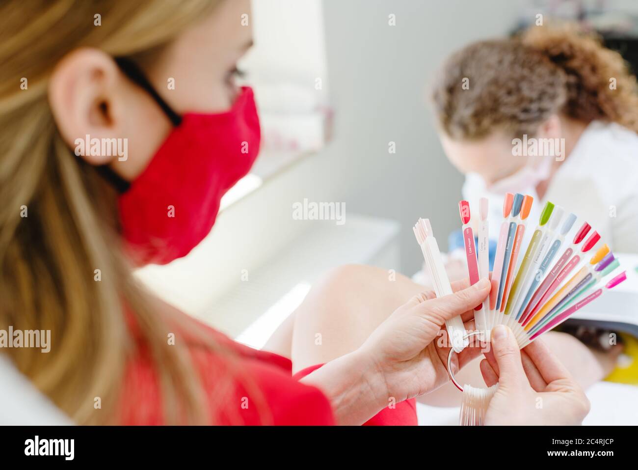 Donna che indossa maschera viso che controlla i colori per pedicure toenail Foto Stock
