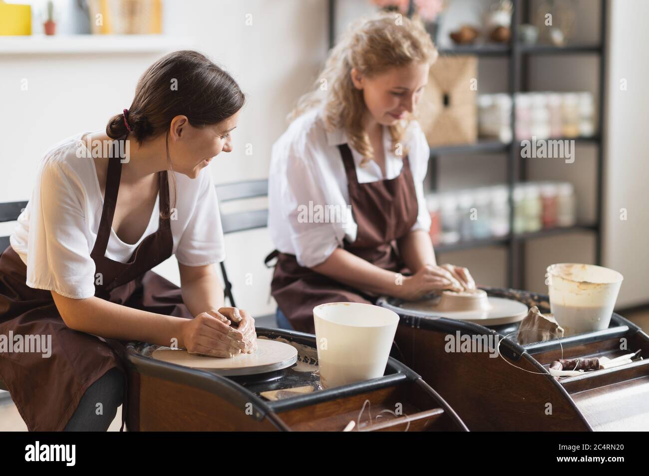 Primo piano di mani di Potter in azione modellando creta di terra cruda usando acqua su ruota di vasaio in movimento a officina di ceramica. Foto Stock