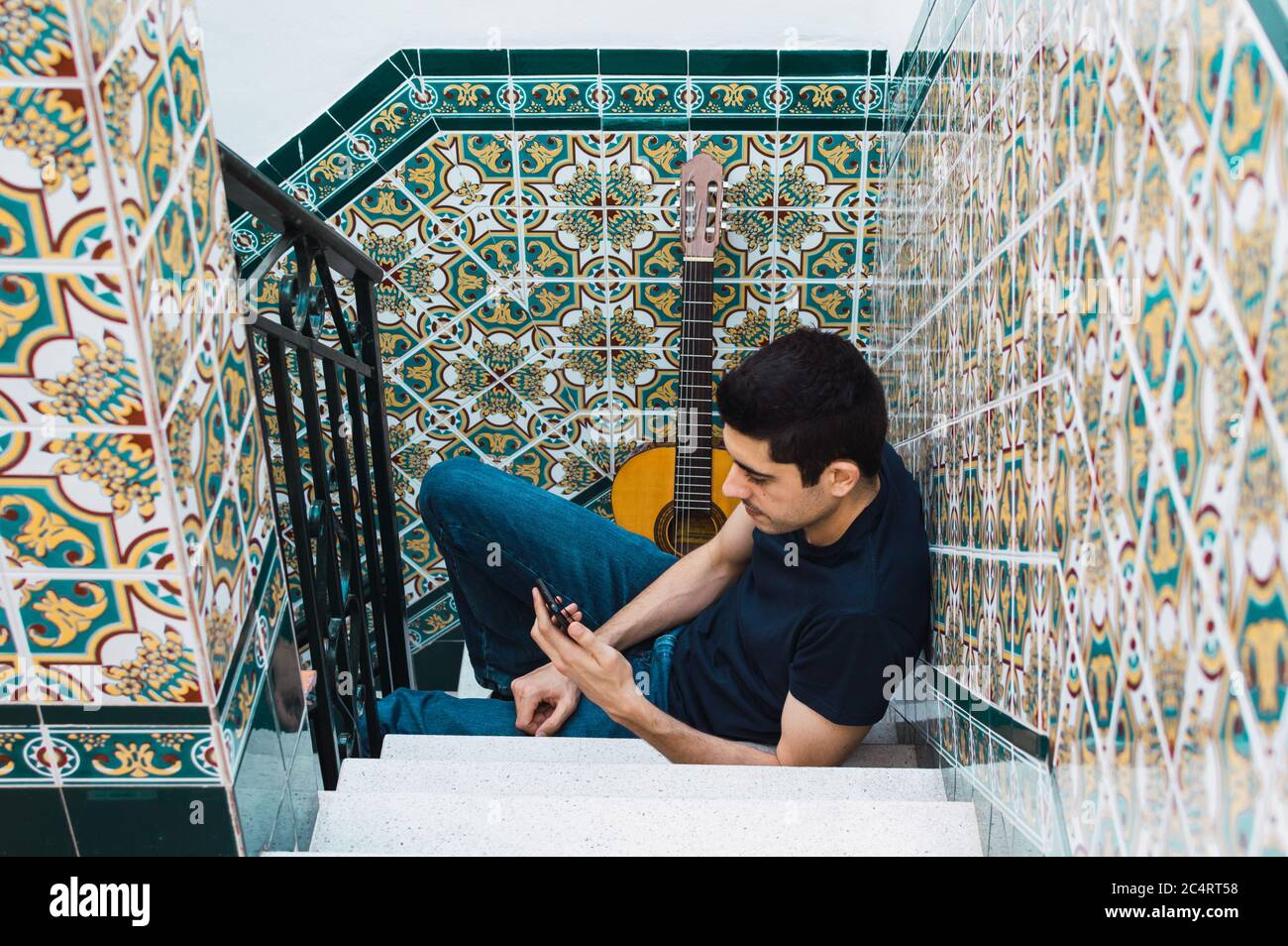 Uomo che usa uno smartphone mentre si riposa dal suonare la chitarra a casa. Foto Stock